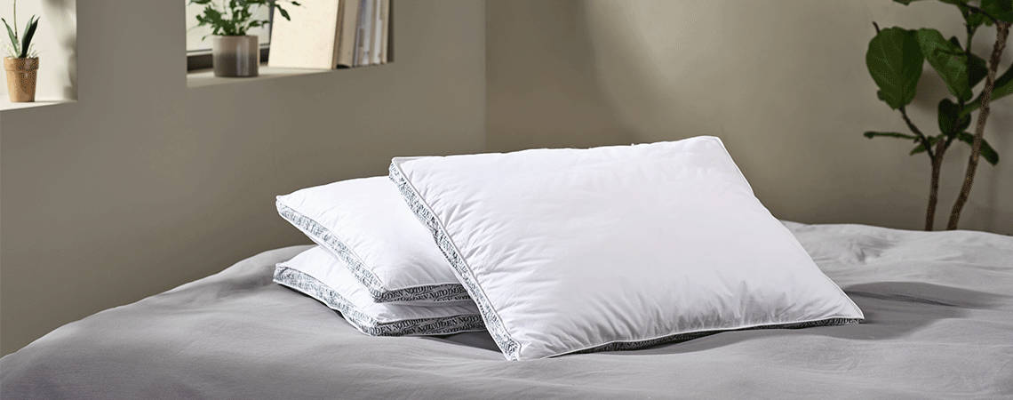 Trois oreillers différents sur un lit avec du linge de lit gris