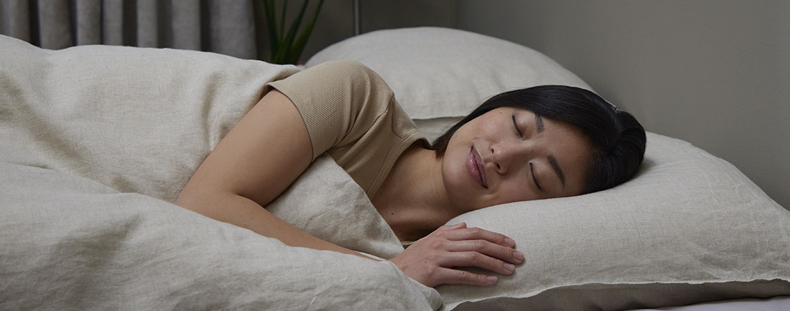 Femme dormant sur le côté dans un lit avec oreiller et couette en lin beige