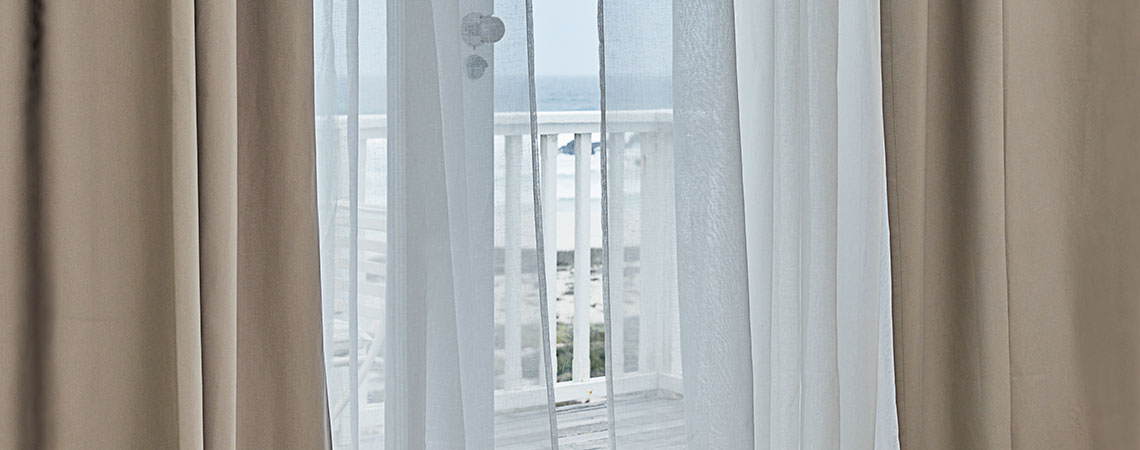 Vue d’un balcon à travers une porte ouverte avec des rideaux flottants