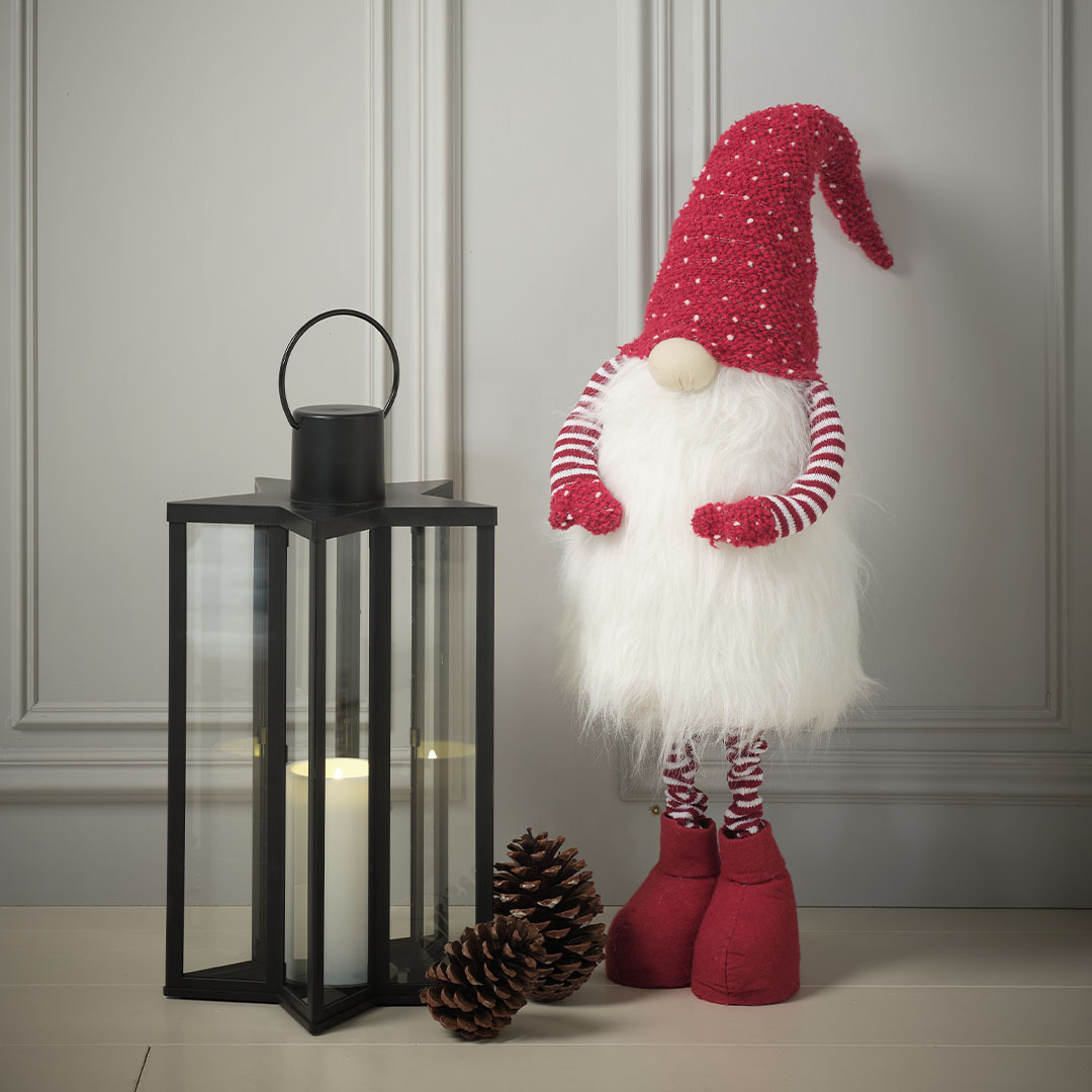 Lutin de Noël NAT et lanterne RHODOLIT Grand lutin de Noël avec un bonnet rouge et une longue barbe à côté d’une lanterne noire en forme d’étoile