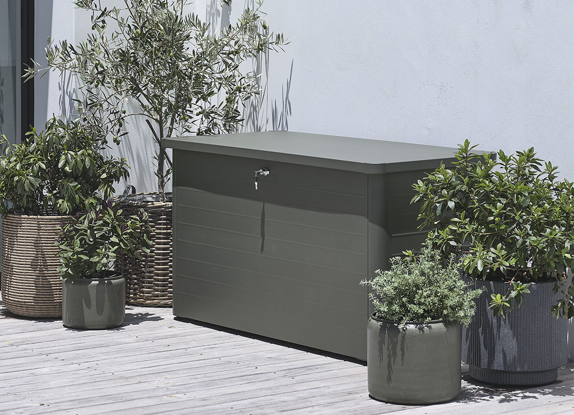 Coffre à coussins DREJET Coffre à coussins de jardin gris sur un patio avec des plantes et des bacs à fleurs