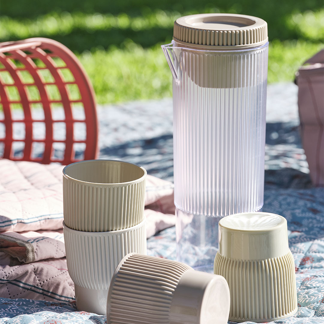 Carafe de pique-nique TJIM avec quatre tasses assorties Essentiels de pique-nique, y compris une carafe avec quatre tasses assorties sur une couverture de pique-nique