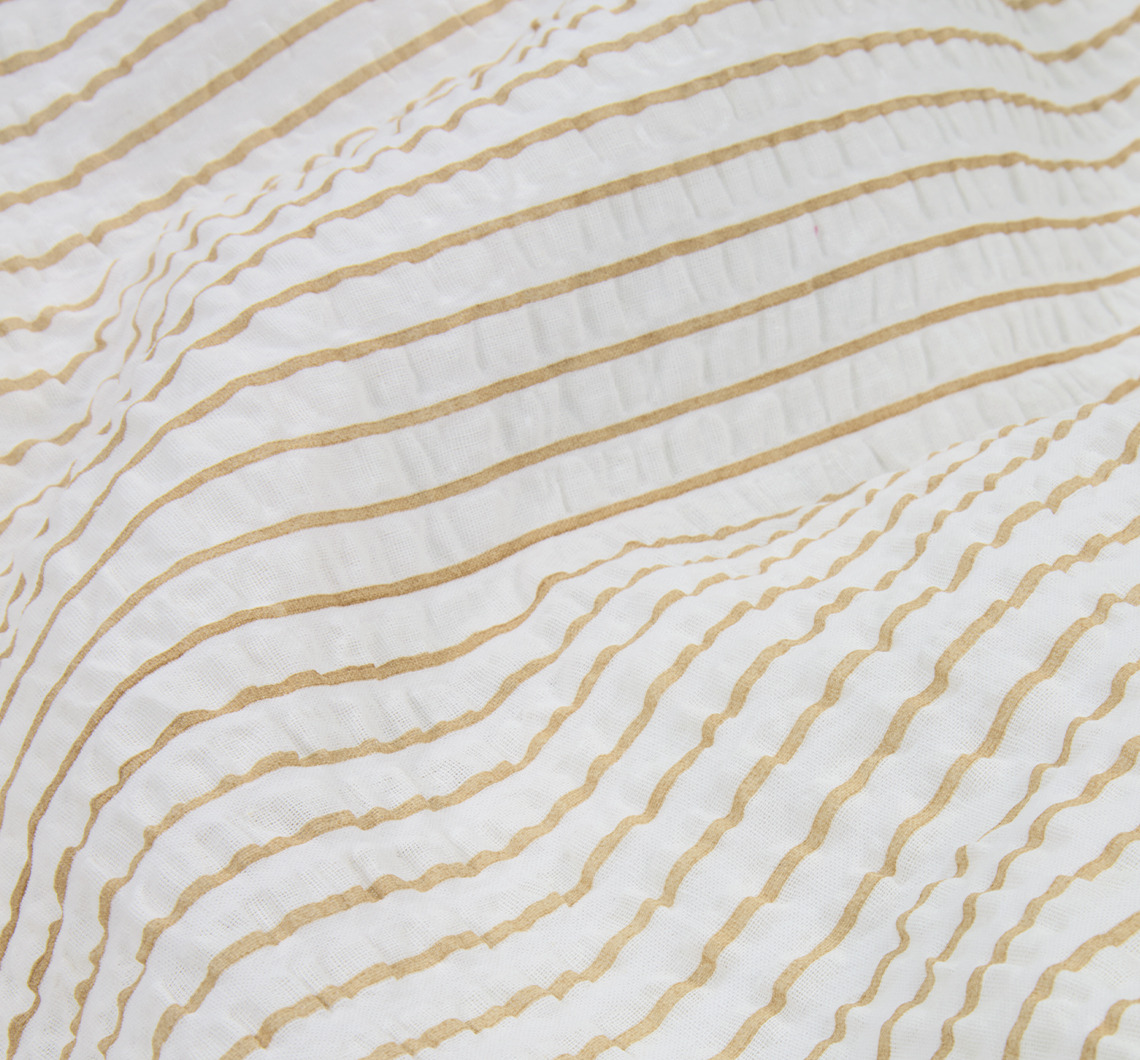 La parure de lit STINNE est décorée de rayures latte et blanches. Gros plan sur du linge de lit à rayures