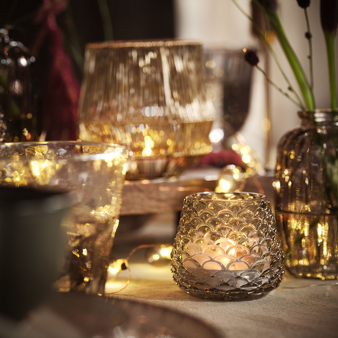 Table à manger éclairée par des bougies et des bougies chauffe-plat dans des photophores et des guirlandes lumineuses