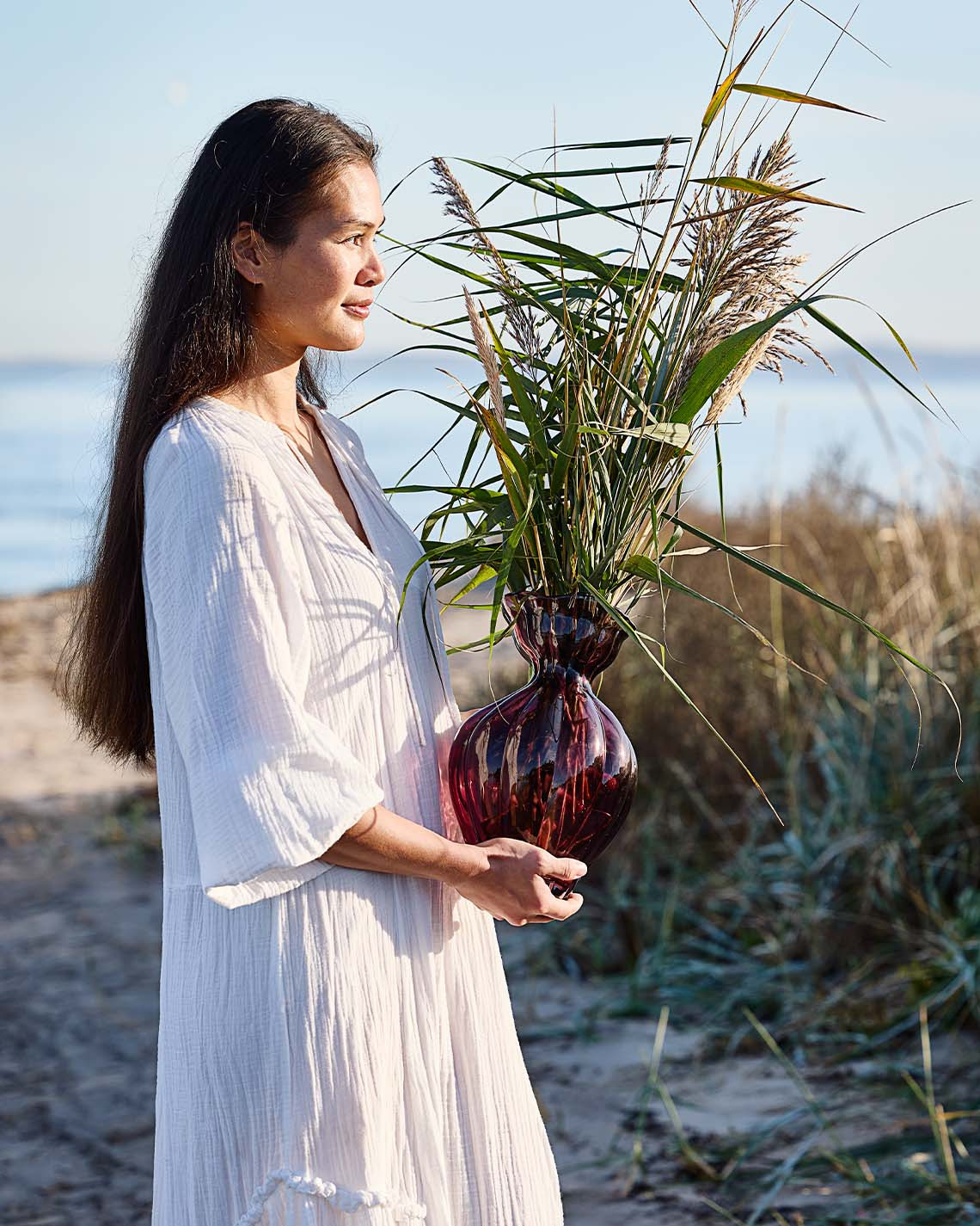 Femme tenant un vase en verre de forme organique sur la plage