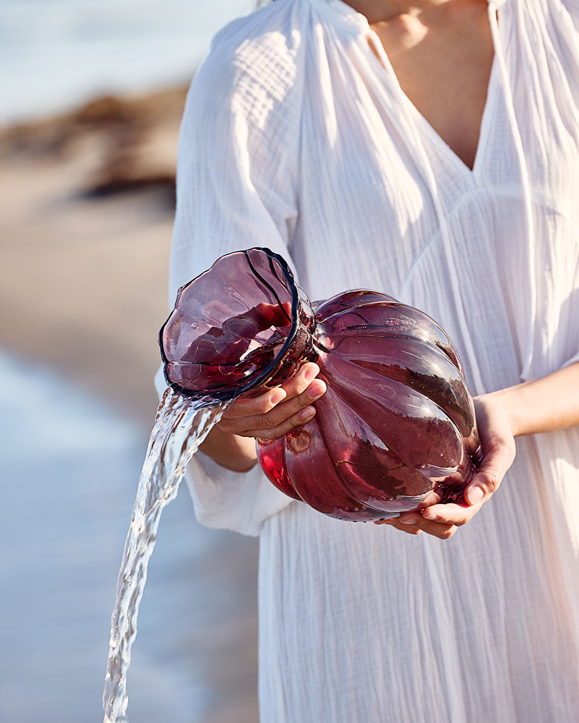 Vase en verre couleur aubergine tenu par une femme sur la plage