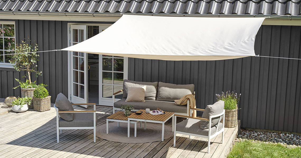 Voile d'ombrage HOLD-AN en coloris blanc Grande voile d’ombrage blanche installée au‑dessus d’une terrasse avec une table de jardin et des chaises de jardin