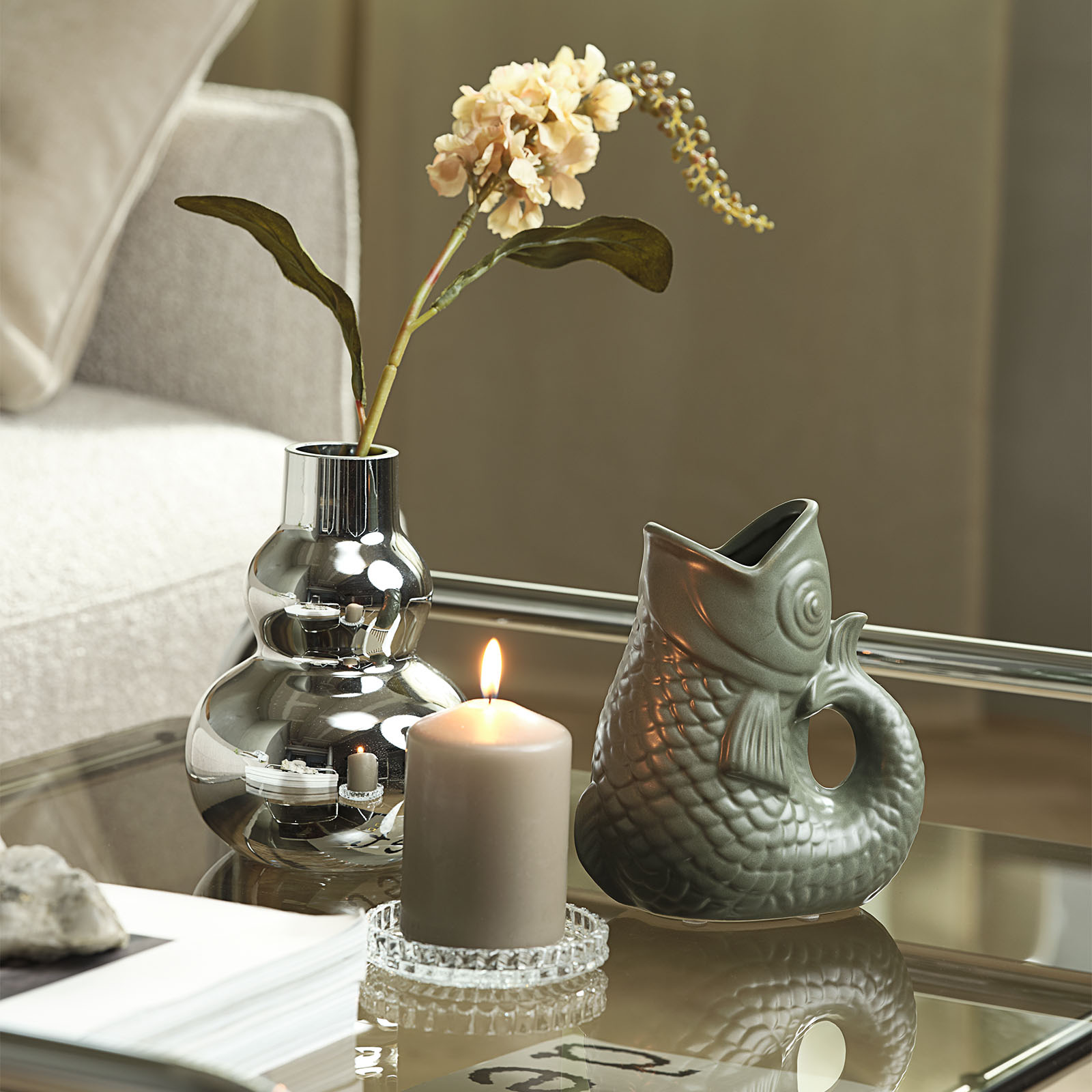 Vase effet chrome avec vase en forme de poisson et bougie sur une table basse